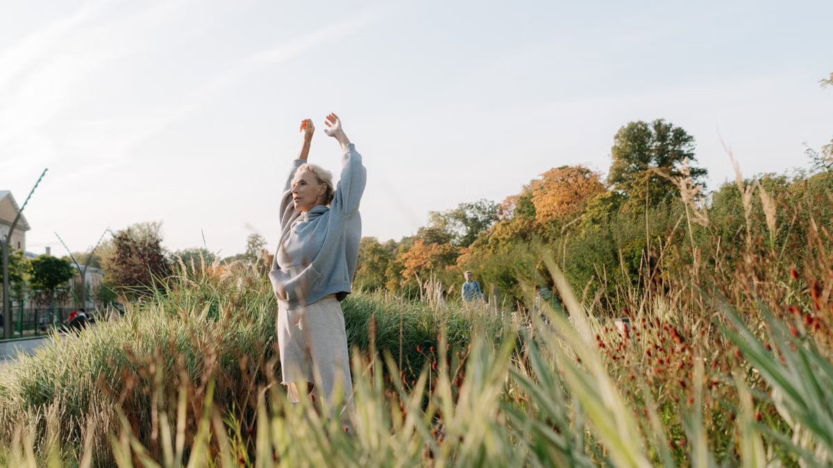 Senior woman enjoying stretching exercises in a lush green park.